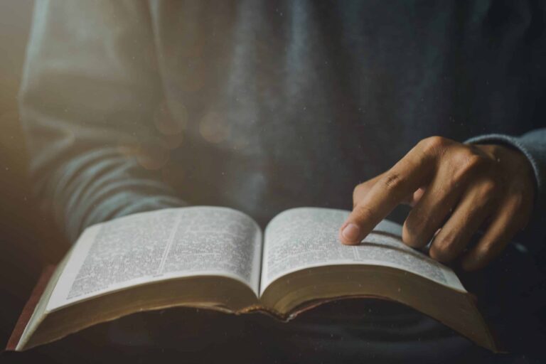 Primer plano de las manos de un hombre cristiano mientras lee la Biblia afuera, domingo.